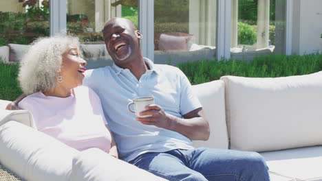 Loving-Retired-Couple-Sitting-Outdoors-At-Home-Having-Morning-Coffee-Together