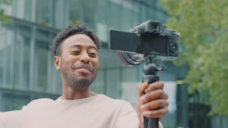 Young-Man-Travelling-Through-City-Vlogging-To-Video-Camera-On-Handheld-Tripod