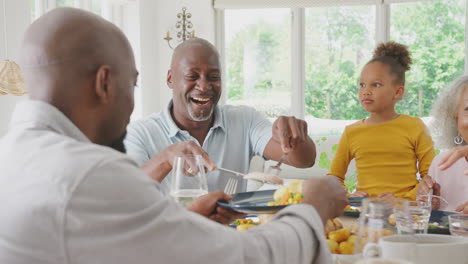 Grandfather-Carving-As-Multi-Generation-Family-Sit-Around-Table-At-Home-And-Enjoy-Eating-Meal