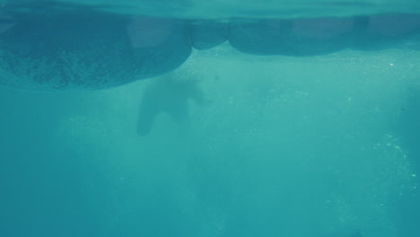 Unterwasseraufnahme-Einer-Mutter,-Die-Entspannt-Auf-Der-Luftmatratze-Im-Schwimmbad-Liegt,-Während-Jungen-Hineinspringen-Und-Sie-Bespritzen