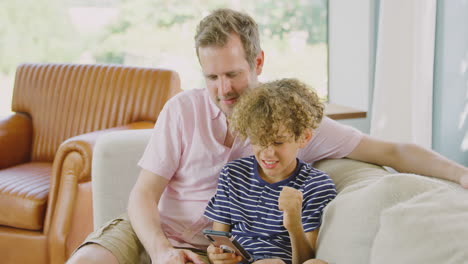 Vater-Und-Sohn-Sitzen-Zu-Hause-Auf-Dem-Sofa-Und-Spielen-Gemeinsam-Ein-Videospiel-Auf-Dem-Handy