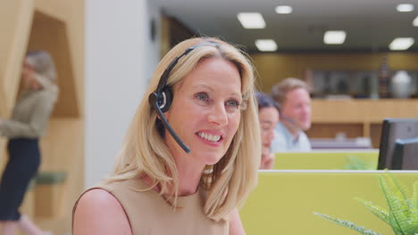 Portrait-Of-Mature-Businesswoman-Wearing-Headset-Talking-To-Caller-In-Customer-Services-Centre