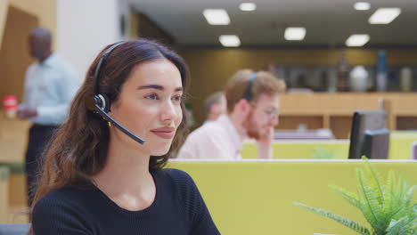 Portrait-Of-Businesswoman-Wearing-Headset-Talking-To-Caller-In-Customer-Services-Centre