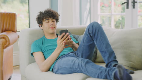 Teenager-Mit-Kabellosen-Ohrhörern-Posiert-Zu-Hause-Mit-Dem-Mobiltelefon-Für-Ein-Selfie-Auf-Dem-Sofa