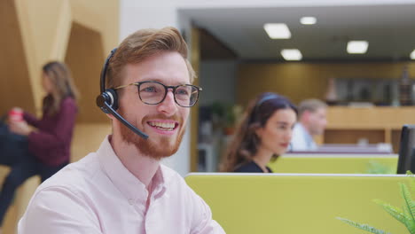 Portrait-Of-Businessman-Wearing-Headset-Talking-To-Caller-In-Customer-Services-Centre
