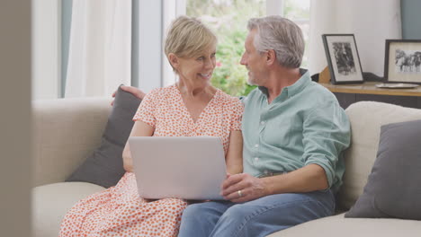 Senior-Retired-Couple-Sitting-On-Sofa-At-Home-Shopping-Or-Booking-Holiday-On-Laptop