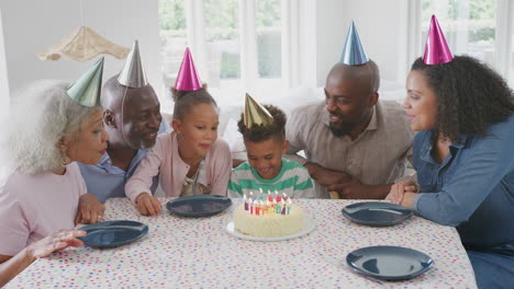 Familia-Multigeneracional-Sentada-Alrededor-De-Una-Mesa-En-Casa-Celebrando-El-Cumpleaños-Del-Niño-Con-Pastel-Y-Fiesta