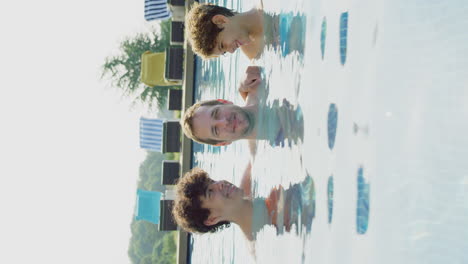 Vertical-Video-Of-Father-With-Sons-Having-Fun-In-Outdoor-Swimming-Pool-On-Summer-Vacation-Together