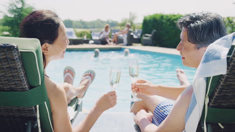 Älteres-Paar-Entspannt-Sich-Im-Sommerurlaub-Am-Pool-Und-Trinkt-Champagner