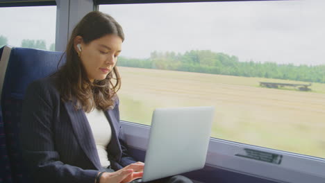 Businesswoman-With-Wireless-Earbuds-Commuting-To-Work-On-Train-Working-On-Laptop