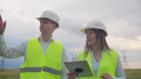 Power-lines-man-and-woman-engineers-with-a-tablet-in-their-hands-check-the-progress-of-the-installation-of-new-towers-and-analyze-the-network