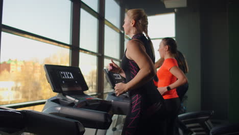A-young-beautiful-woman-and-three-people-running-on-a-treadmill-in-a-fitness-room-performing-a-cardio-workout.-Indoor-running-warm-up-before-training-in-slow-motion.