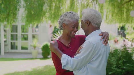 Loving-Senior-Couple-Standing-In-Garden-At-Home-And-Hugging-After-Retirement