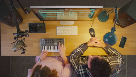 Overhead-View-Of-Male-And-Female-Musicians-At-Computer-With-Keyboard-In-Studio-At-Night