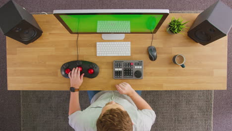 Overhead-View-Of-Male-Video-Editor-Working-At-Computer-With-Green-Screen-In-Creative-Office