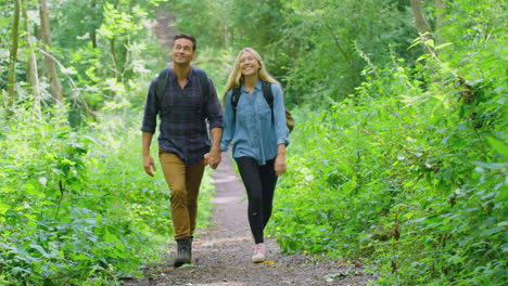 Loving-Couple-In-Countryside-Hiking-Along-Path-Through-Forest-Holding-Hands-Together