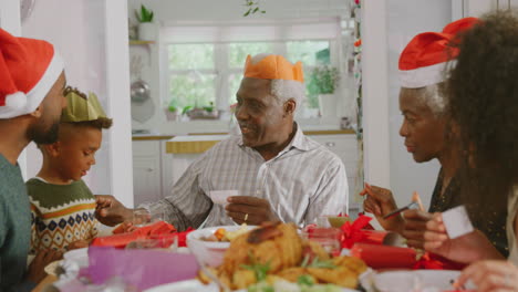 Mehrgenerationenfamilie-Mit-Papierhüten,-Die-Weihnachtscracker-Witze-Liest,-Während-Sie-Gemeinsam-Isst