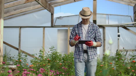 Young-entrepreneur-hothouse-owner-is-doing-inventory-in-greenhouse-counting-plants-and-entering-information-in-tablet.-Attractive-man-is-busy-checking-greenery.
