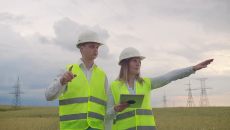 Power-lines-a-man-and-a-woman-engineers-with-a-tablet-in-their-hands-discussing-the-progress-of-the-construction-project