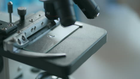 Nahaufnahme-Eines-Mikroskopokulars,-Das-Auf-Eine-Probe-Auf-Einem-Stück-Glas-Gerichtet-Ist.-Nahaufnahme-Von-Probenobjektträger-Und-Mikroskop-Mit-Metalllinse-Im-Labor.-Hochwertiges-4K-Filmmaterial