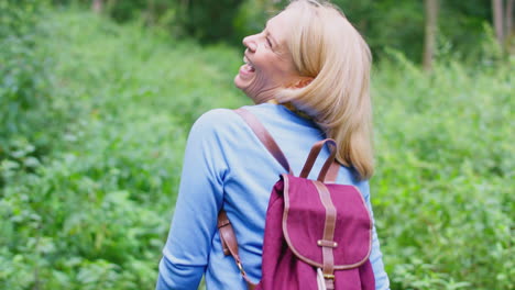 Rear-View-Of-Mature-Woman-Wearing-Backpack-In-Countryside-Hiking-Along-Path-Through-Forest