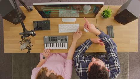 Overhead-View-Of-Male-And-Female-Musicians-At-Workstation-With-Keyboard-And-Microphone-In-Studio