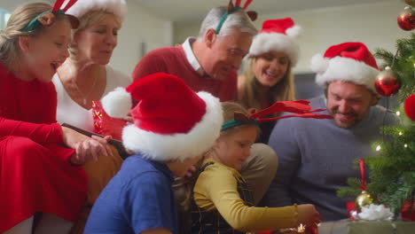 Familia-Multigeneracional-Intercambiando-Y-Abriendo-Regalos-Alrededor-Del-árbol-De-Navidad-En-Casa