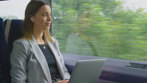 Businesswoman-With-Wireless-Earbuds-Commuting-To-Work-On-Train-Working-On-Laptop