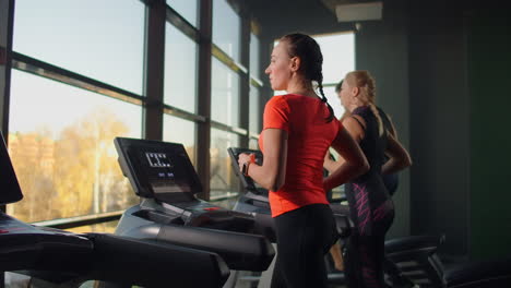 Cute-young-girl-running-on-a-treadmill-in-front-of-panoramic-Windows-in-the-fitness-room.-Gym-with-treadmill-and-large-Windows.