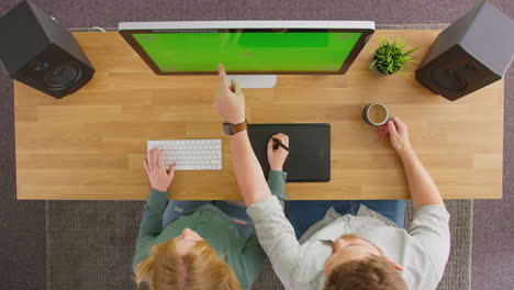 Overhead-View-Of-Male-And-Female-Graphic-Designers-Working-At-Computer-With-Green-Screen-In-Office
