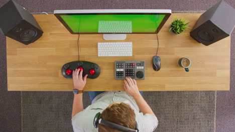 Overhead-View-Of-Frustrated-Male-Video-Editor-Working-At-Computer-With-Green-Screen-In-Office