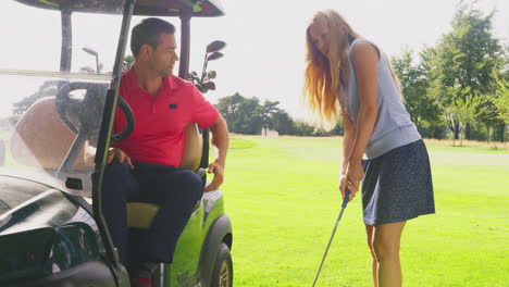 Mann-Im-Golfbuggy-Gibt-Einer-Frau-Ratschläge,-Während-Sie-Mit-Dem-Golfschläger-Trainiert