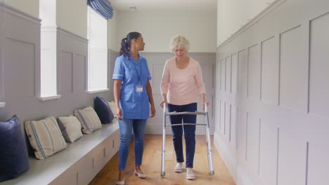 Senior-Woman-At-Home-Using-Walking-Frame-Being-Helped-By-Female-Care-Worker-In-Uniform