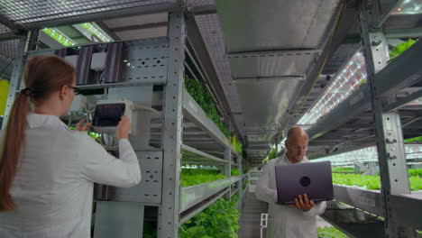 Scientists-in-white-coats-with-a-laptop-and-a-tablet-analyzes-the-work-of-a-vertical-farm-to-grow-pure-unmodified-products-in-an-automated-farm.-The-camera-moves-on-the-site-on-gimbal.
