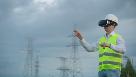 Middle-plan-male-energy-engineer-in-virtual-reality-glasses-and-white-helmet-on-the-background-of-high-voltage-power-line-towers.