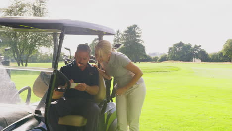 Mature-Couple-Playing-Round-On-Golf-Together-Sitting-In-Buggy-With-Score-Card