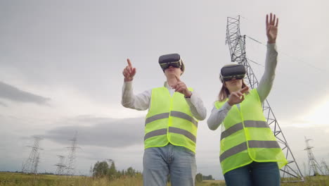 A-man-and-a-woman-engineer-in-VR-glasses-control-the-power-distribution-of-electric-networks-and-the-delivery-of-electricity-against-the-background-of-electric-towers-with-high-voltage-cables