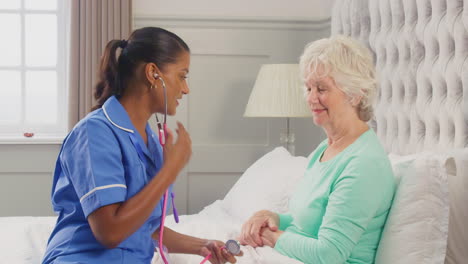 Pflegerin-In-Uniform-Hört-Zu-Hause-Im-Bett-Mit-Stethoskop-Auf-Die-Brust-Einer-älteren-Frau