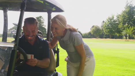 Mature-Couple-Playing-Round-On-Golf-Together-Sitting-In-Buggy-With-Score-Card