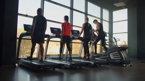 Four-people-young-men-and-women-walking-on-treadmills-in-the-fitness-room.-Start-training-warm-up-people-before-fitness-training.
