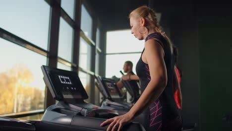 A-woman-walks-up-to-the-treadmill-and-turns-it-on-to-start-training.-Include-a-treadmill-in-the-gym-fitness-room.