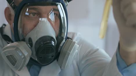 Close-up-in-the-laboratory-a-man-in-a-glass-respirator-screen-holds-a-glass-tube-with-a-yellow-liquid-against-the-virus-and-looks-at-it.-High-quality-4k-footage