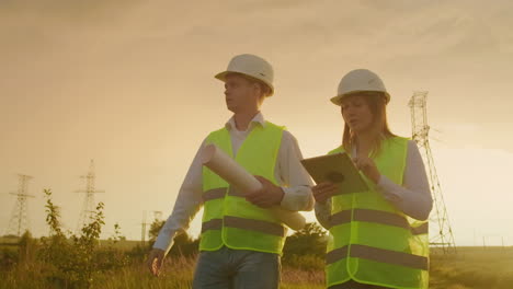 Coworking-engineers-with-tablets-on-solar-plant.-Adult-men-and-women-in-hardhats-using-tablets-while-standing-outdoors-on-transformer-platform.-Transportation-of-clean-energy.-Wind-energy-delivery