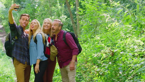 Group-Of-Friends-Posing-For-Selfie-In-Countryside-Taking-Picture-On-Phone-As-They-Hike-Along-Path