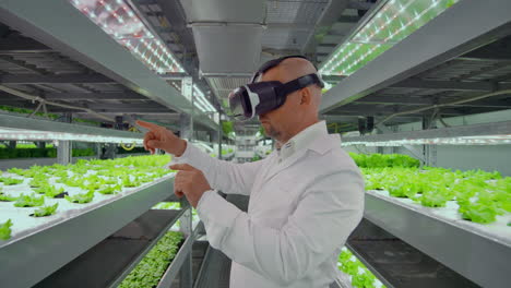 Ein-Moderner-Männlicher-Mikrobiologe-Nutzt-Eine-Virtual-Reality-Brille,-Um-Das-Klima-Auf-Einem-Modernen-Bio-Gemüsebauernhof-Zu-Kontrollieren-Und-Zu-Verwalten.