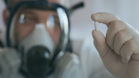 Close-up-in-the-laboratory-a-man-in-a-glass-respirator-screen-holding-a-new-medicine-a-white-pill-an-antibiotic-against-the-virus-and-looking-at-it.-High-quality-4k-footage