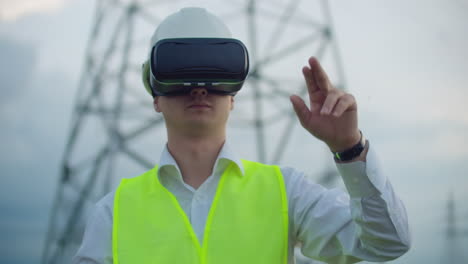 Middle-plan-male-energy-engineer-in-virtual-reality-glasses-and-white-helmet-on-the-background-of-high-voltage-power-line-towers.