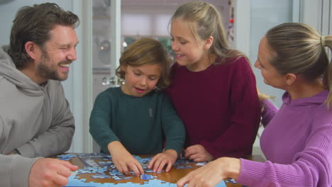 Familie-Mit-Kindern-Sitzt-Zu-Hause-Am-Tisch-Und-Macht-Gemeinsam-Puzzle