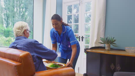 Pflegerin-In-Uniform-Bringt-Einem-älteren-Mann,-Der-Zu-Hause-In-Der-Lounge-Sitzt,-Essen-Auf-Einem-Tablett