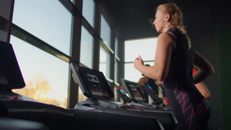 Cute-young-girl-running-on-a-treadmill-in-front-of-panoramic-Windows-in-the-fitness-room.-Gym-with-treadmill-and-large-Windows.